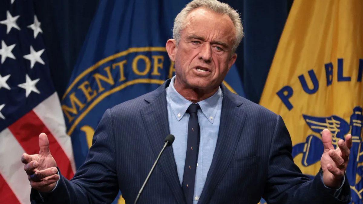 A white man wearing a blue suit speaks at a microphone.
