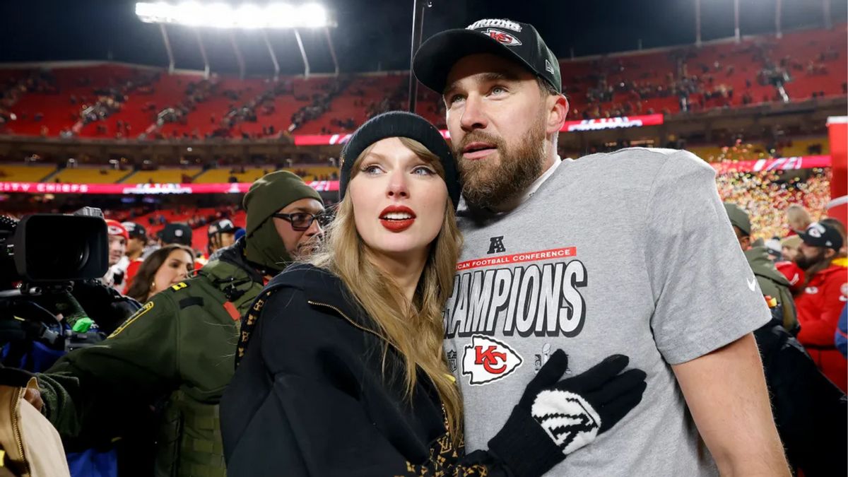 A white woman and man look towards the left while standing in a stadium. People surround them.