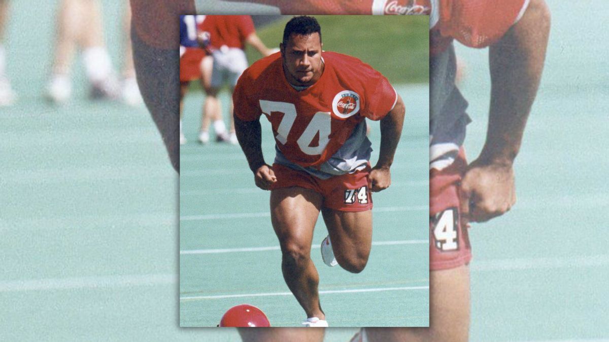 A Black/Samoan man moves towards the camera wearing a red uniform with the number 74 on it.