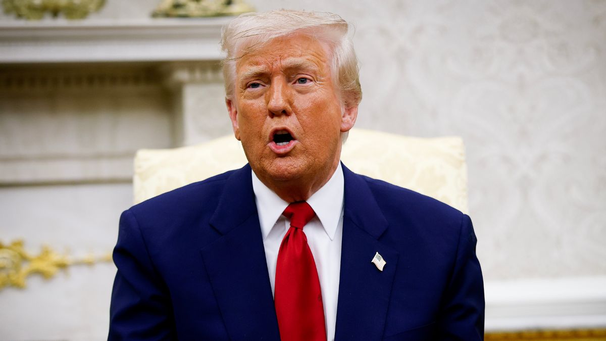A white man wearing a blue suit speaks while sitting down.
