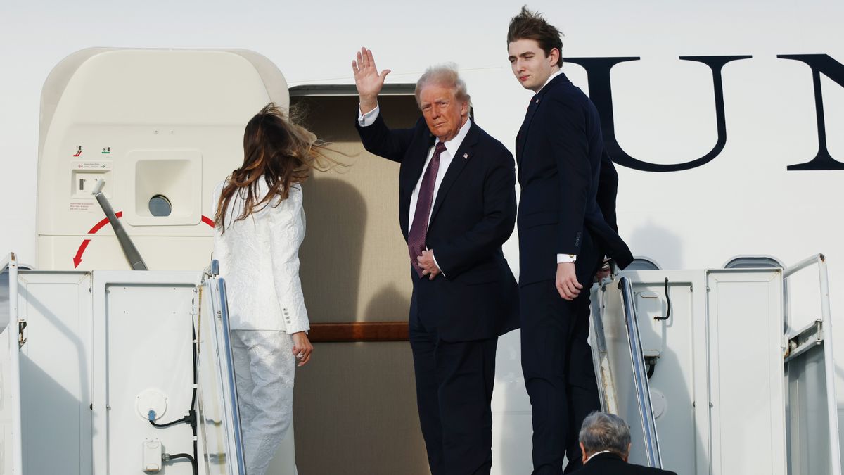 A white man turns to wave at the entrance to a plane. A white woman and man stand to his left and right respectively.