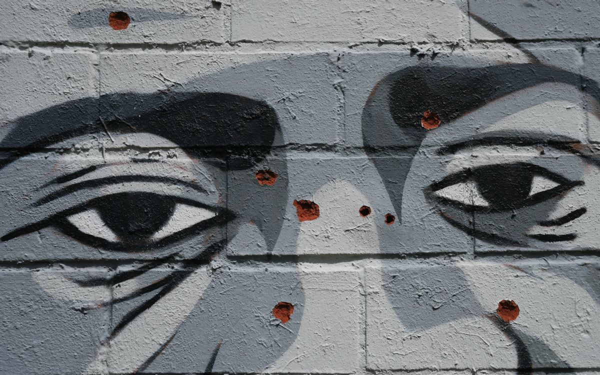 A gray mural with a Black man's eyes is shown. There are red spots on the mural that make it look like someone has tried to destroy it.