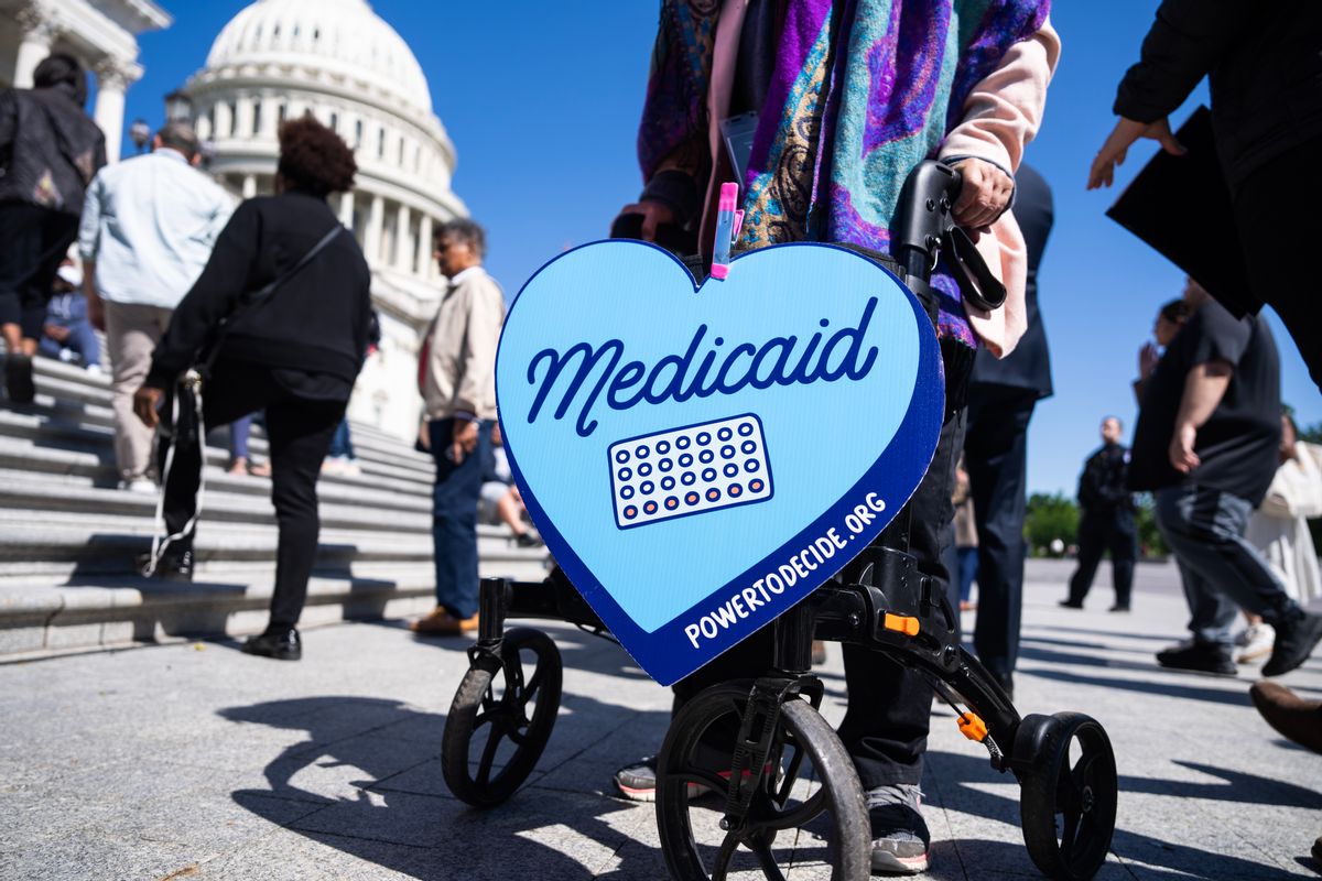 A blue sign shaped like a heart that says "Medicaid" hangs from a person's walker outside the U.S. Capitol building. 