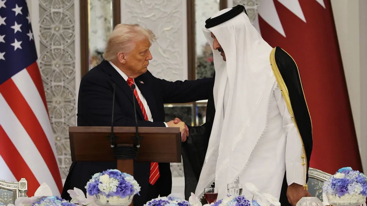 A white man wearing a dark suit stands at a podium. His arm rests on the back of a veiled man standing to his right, who he is looking at.