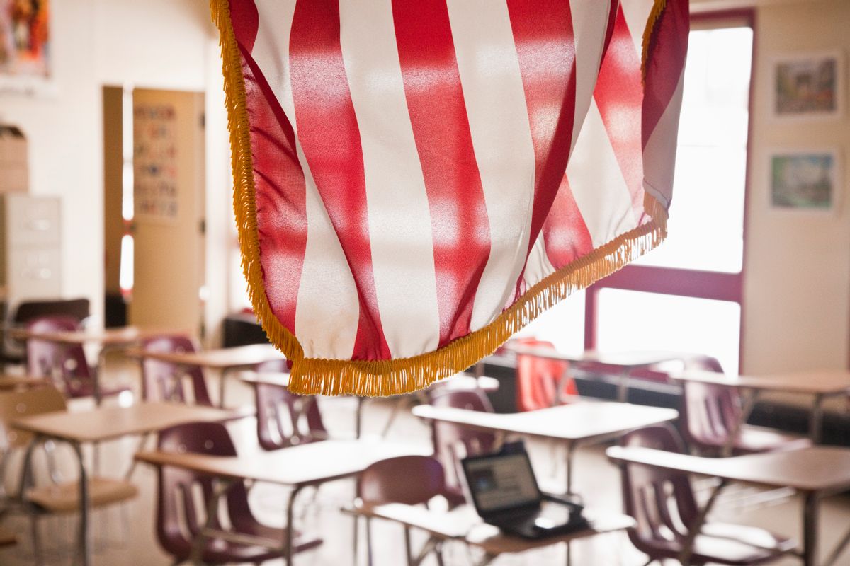 An American flag, with red and white stripes, hangs in front of an empty classroom. 