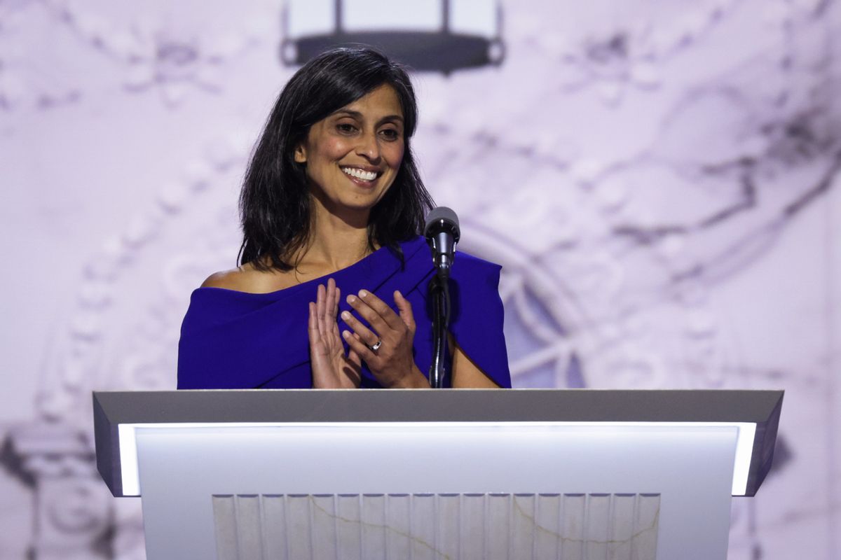 An Indian woman wearing a blue dress stands behind a podium.