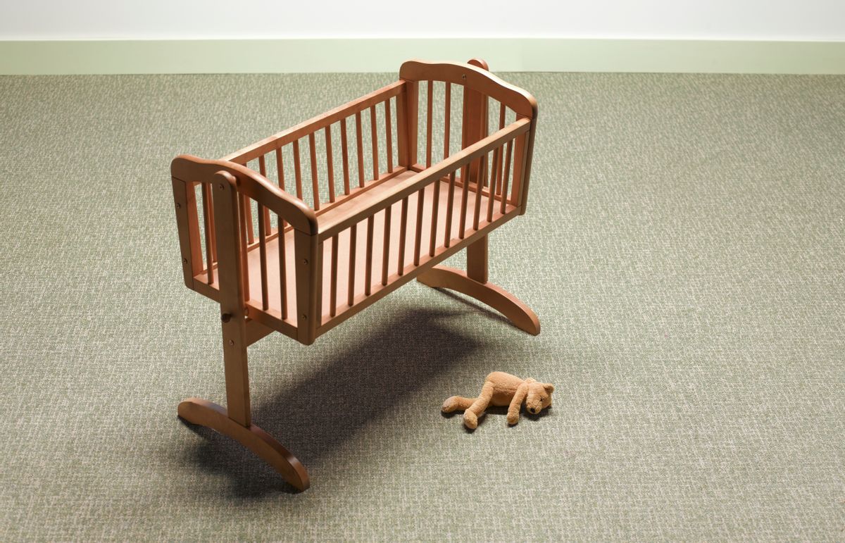 An empty crib with a teddy bear beside it. 