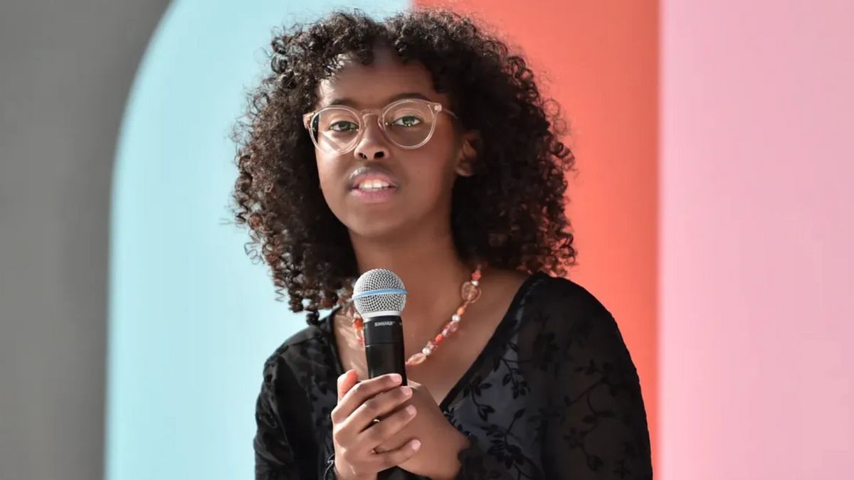 A Black woman holds a microphone while looking forward.