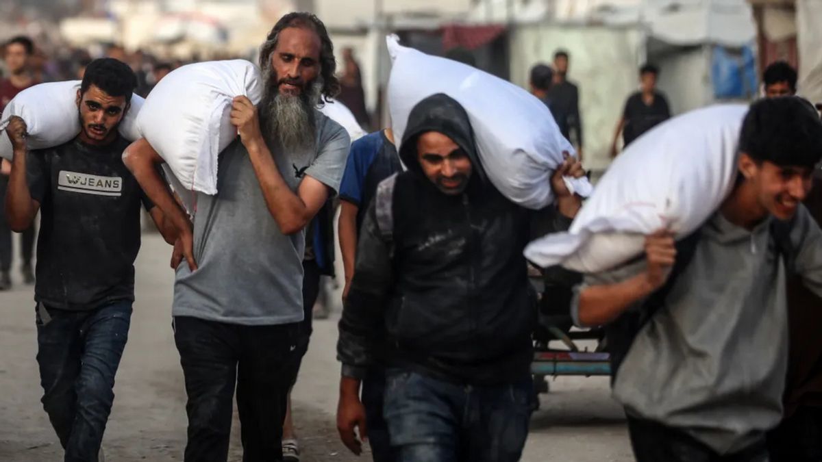 Four Palestinian men carrying flour on their shoulders. 