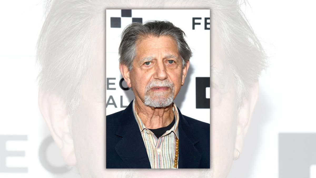 A white man being photographed looks at the camera.