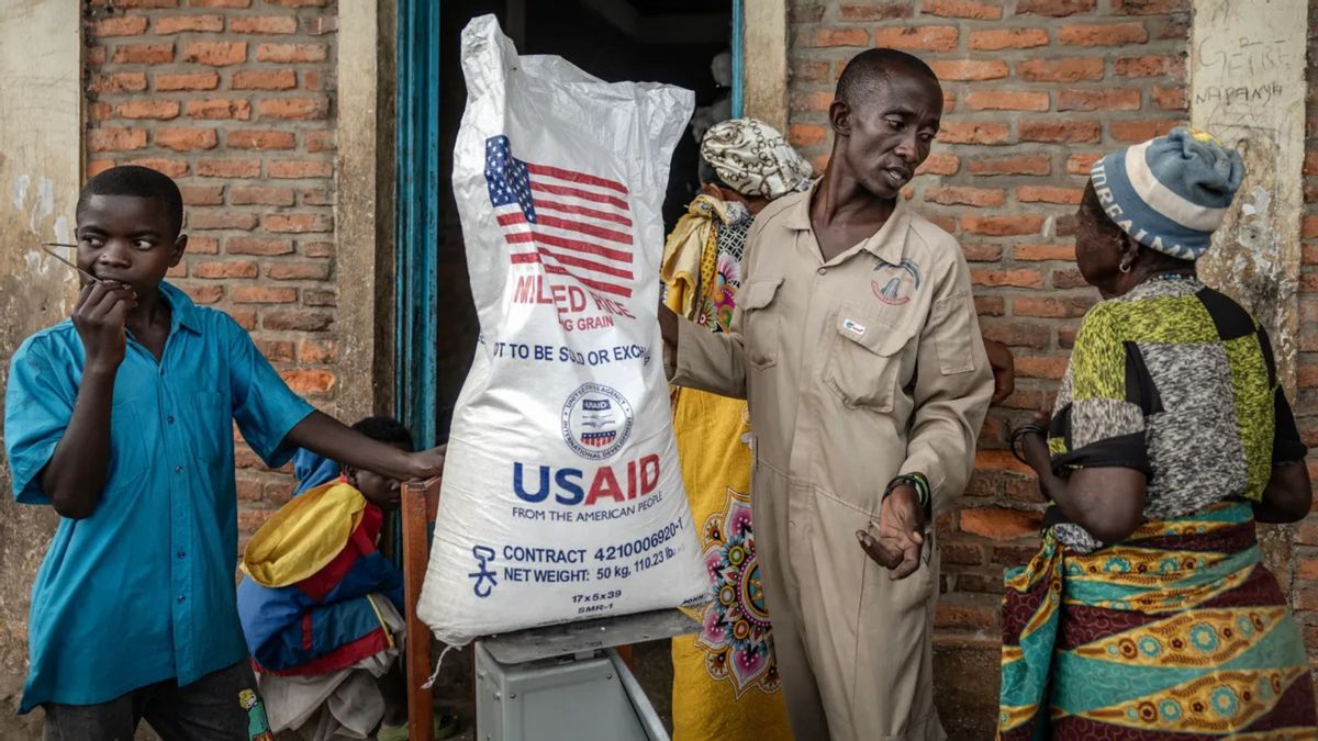 Several Black people stand near a door. One is holding what appears to be a bag that says USAID on it.