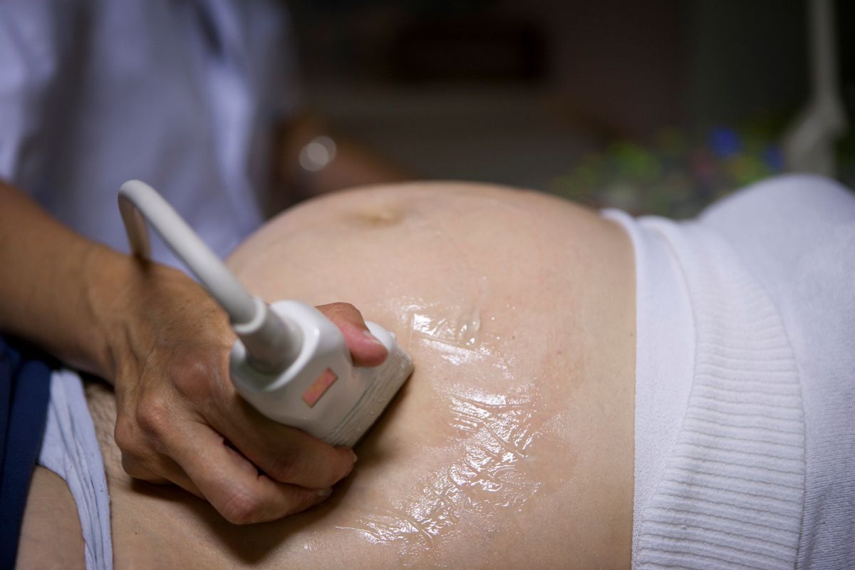 A hand holding an ultrasound device over a pregnant belly. 