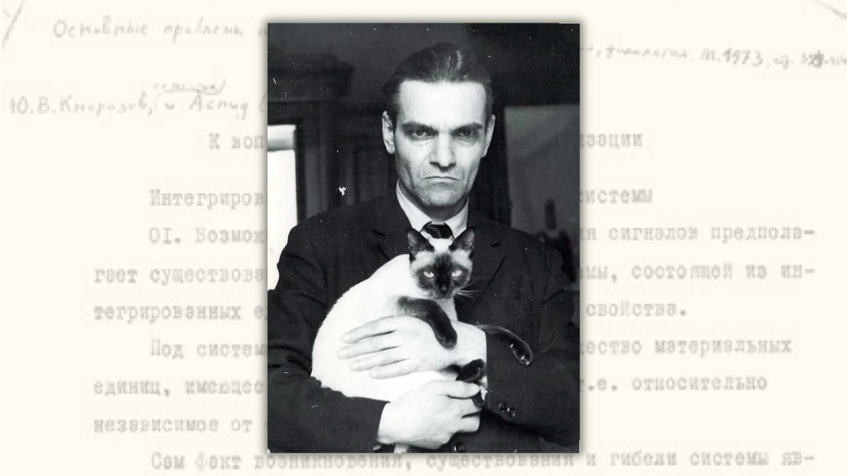 In the foreground: A black and white headshot photo of a stern man holding what appears to be a Siamese cat. In the background: Russian text. 