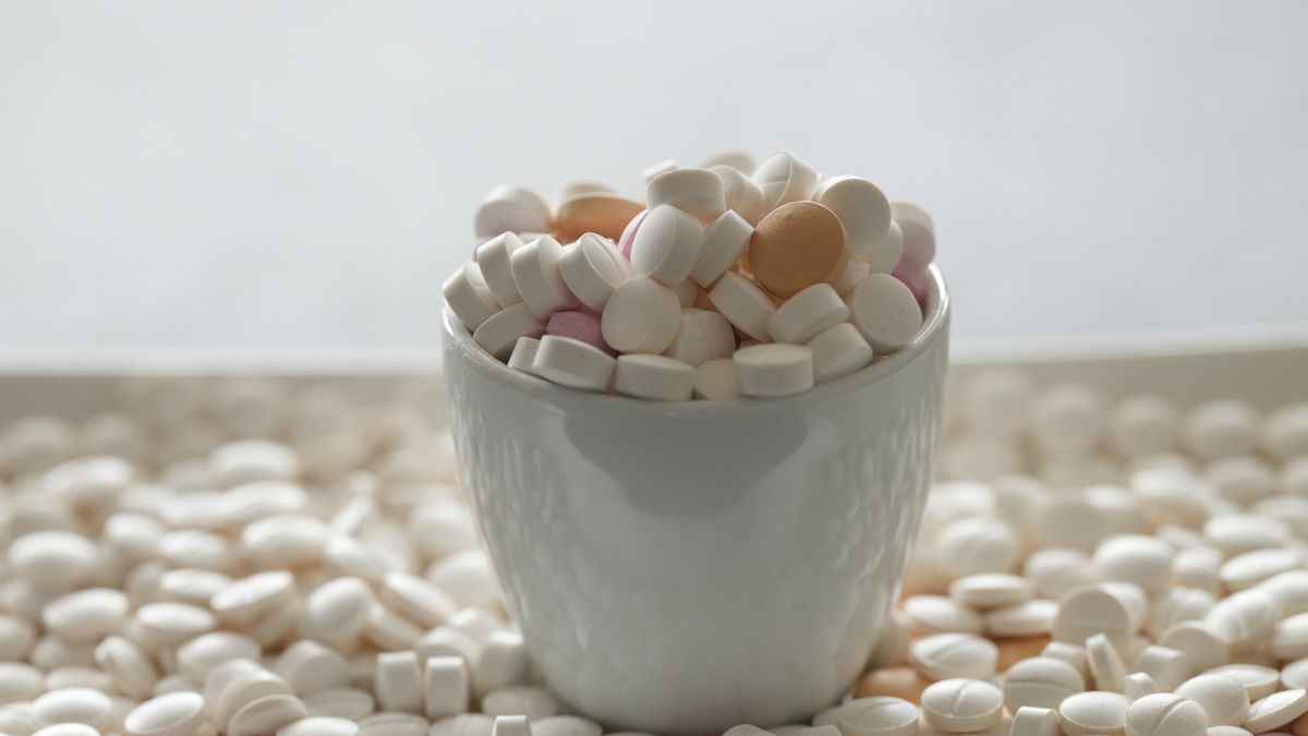 Bunch of different pill tablets in a cup sitting atop more colorful tablets