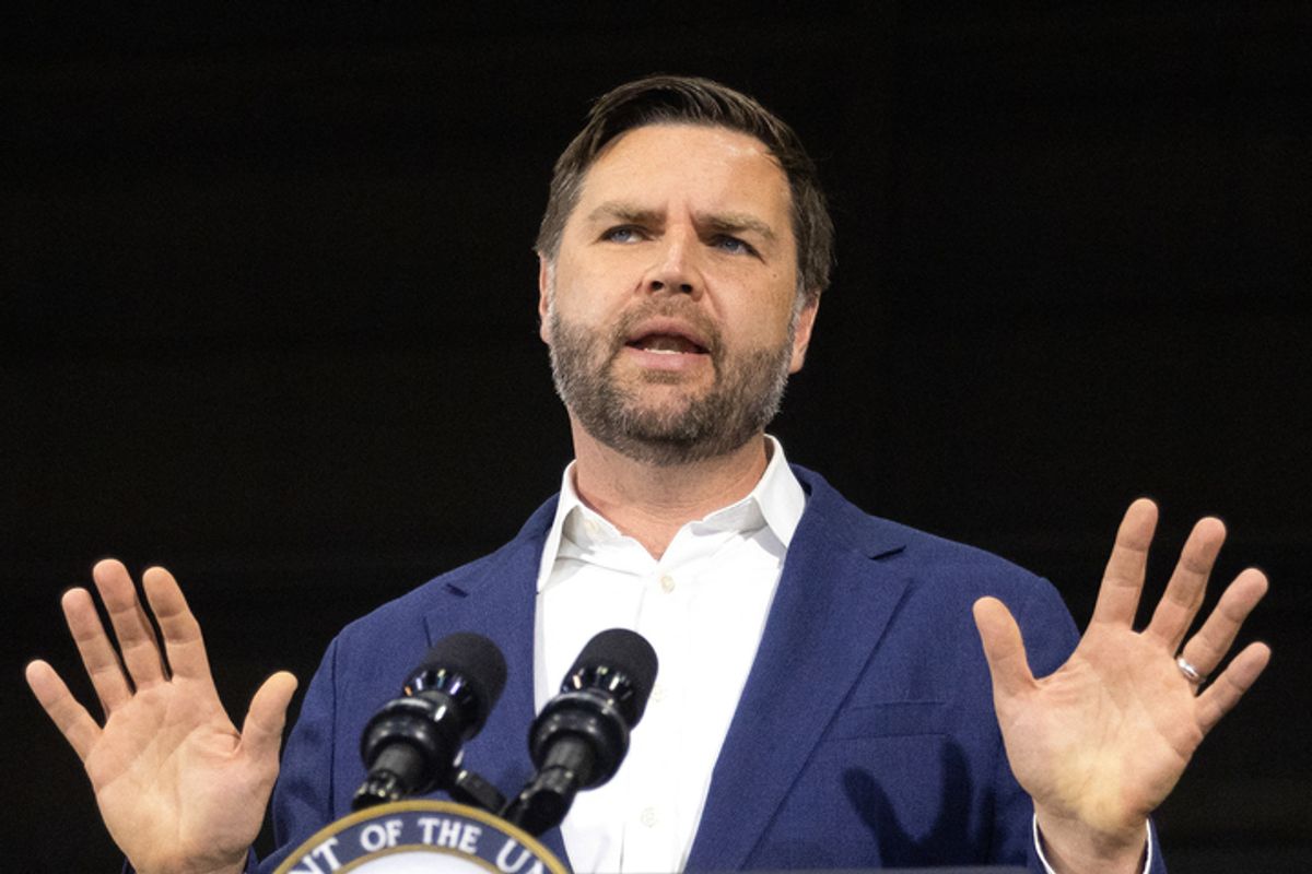 A white man with short cropped brown hair and a beard, U.S. President JD Vance, holds his hands up while speaking in front of a microphone. 