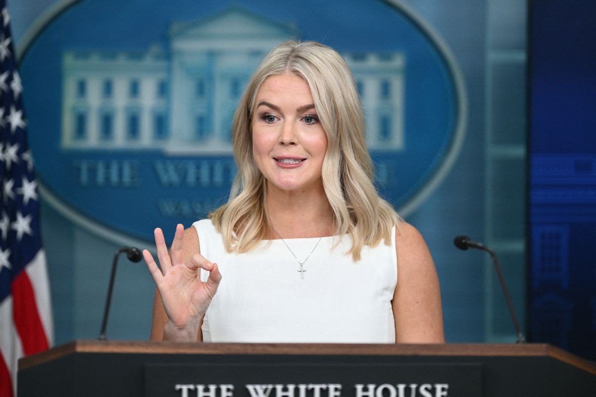 A white woman with shoulder-length blonde hair wearing a cross necklace and a white dress does an "OK" sign with her hands while she talks in front of a White House podium.