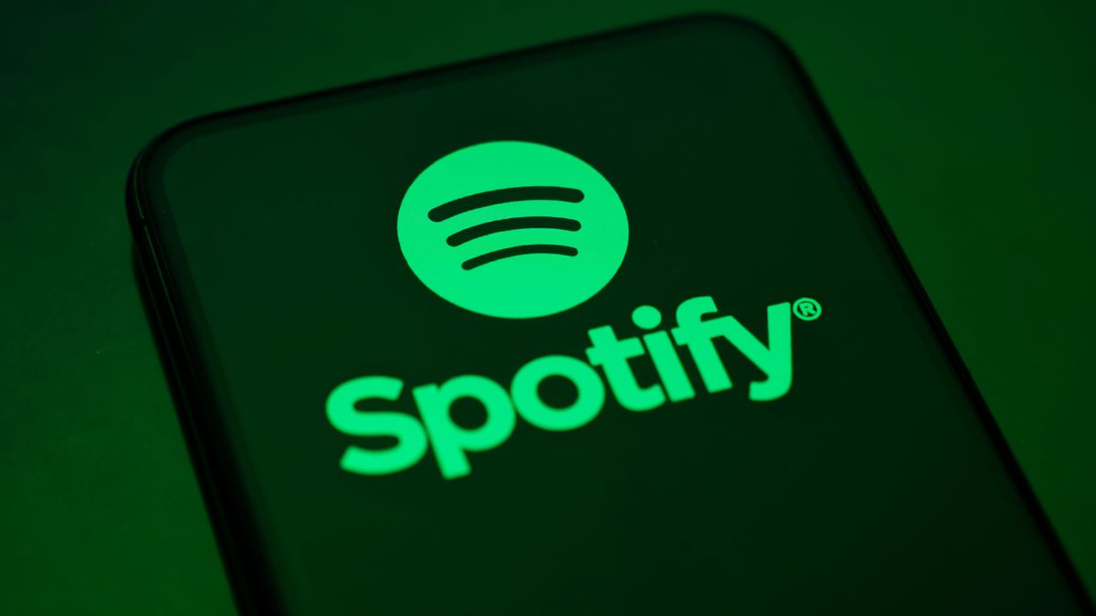 "Spotify" in green text and a green Spotify logo appear on a smartphone reflecting a green light. 