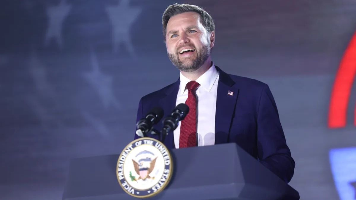 A white man wearing a blue suit speaks while standing at a podium.