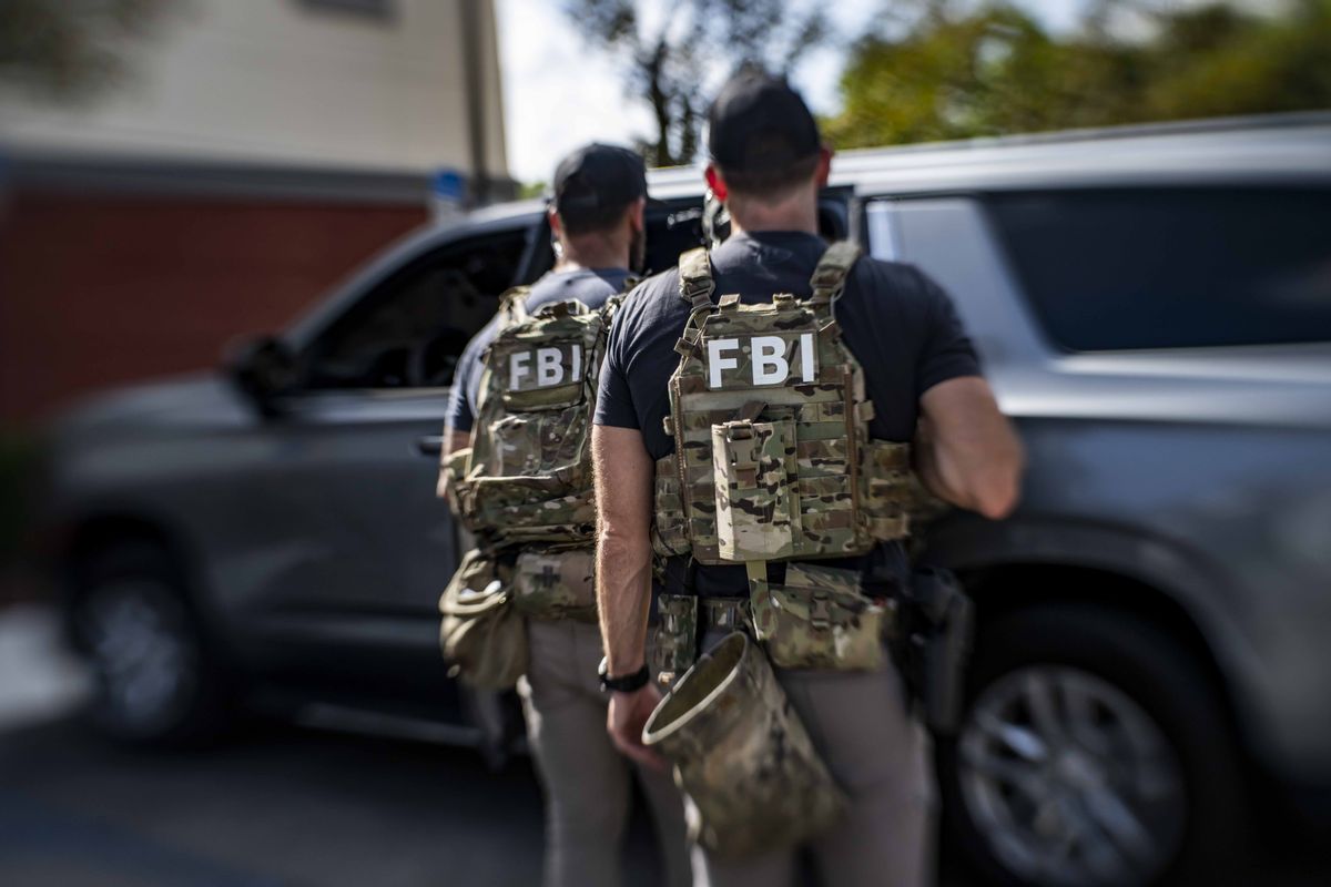 Two FBI agents wearing bulletproof vests walk away from the camera. 