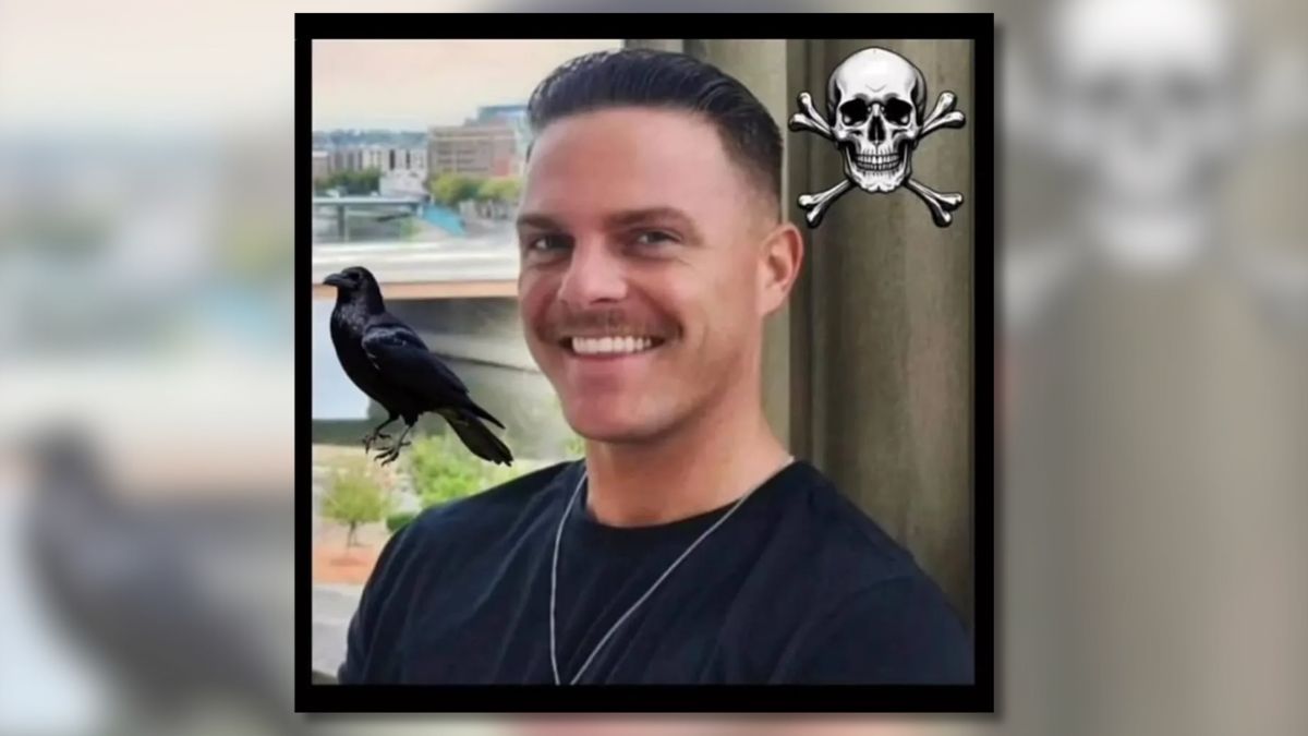 A smiling white man with a mustache wearing a black T-shirt