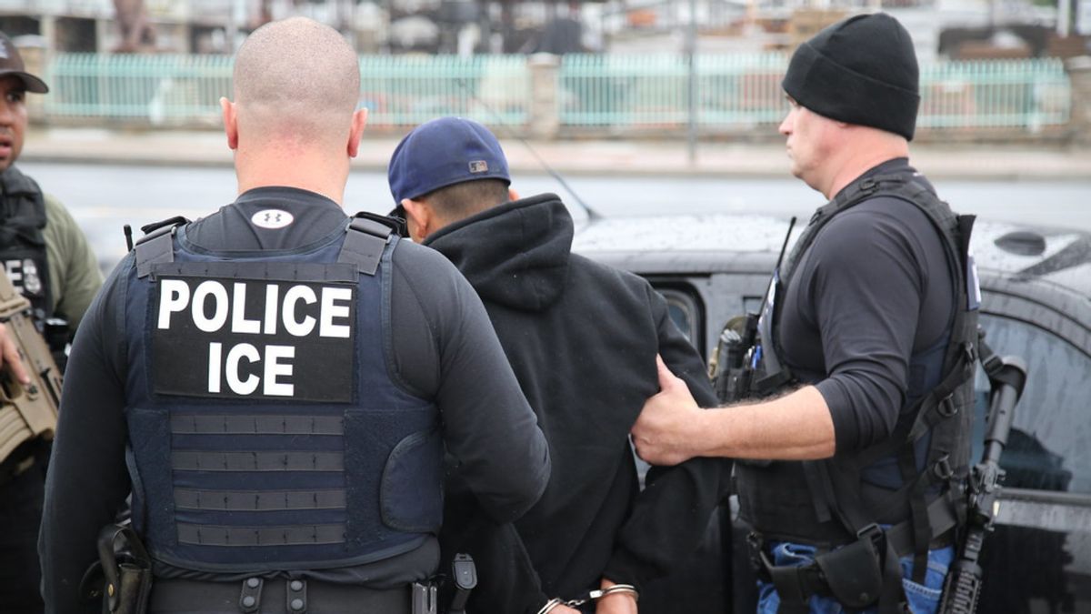Two ICE officers escort a handcuffed man into a car. 