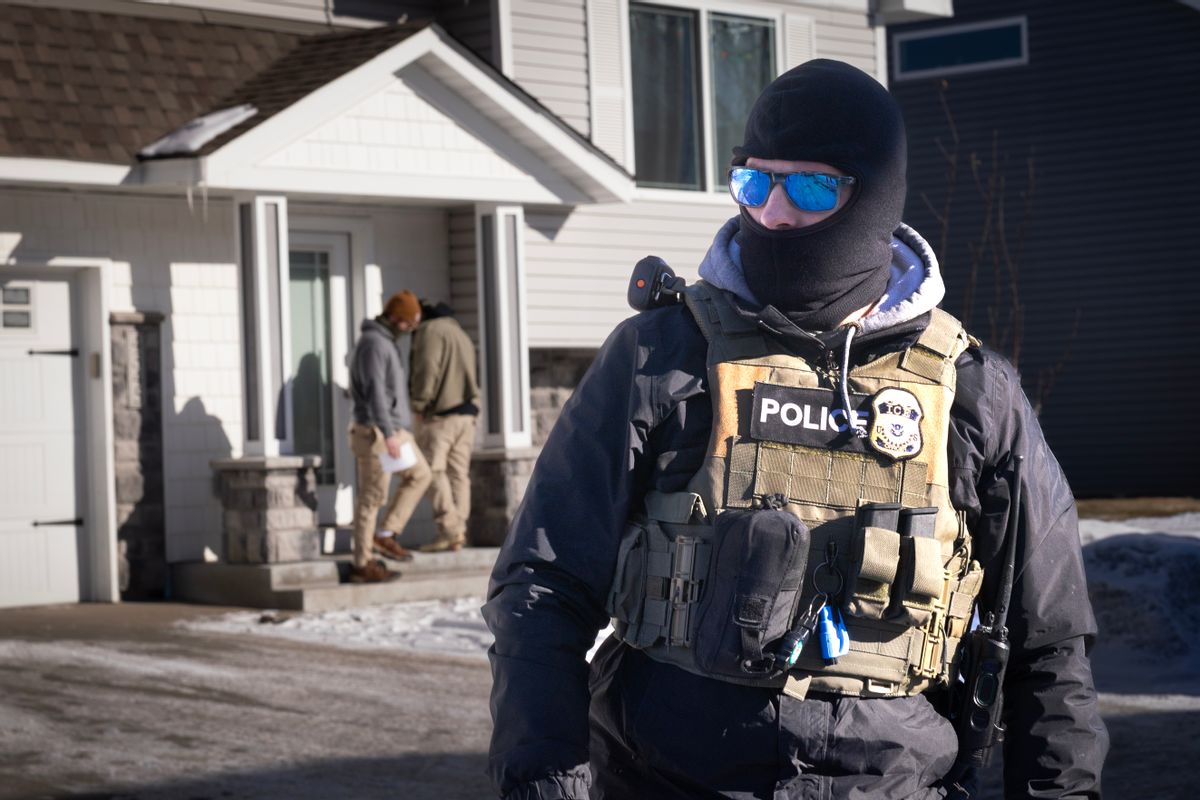 A masked ICE officer outside of a house in the snow.