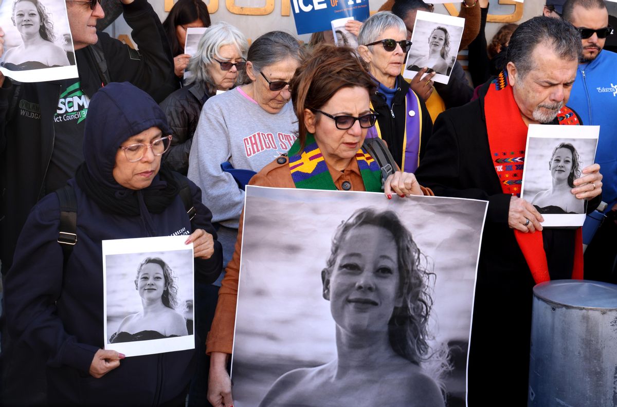 A group of people bow their heads and pray. Some are holding a black and white picture of Renee Nicole Good, a woman with medium-length curly hair.