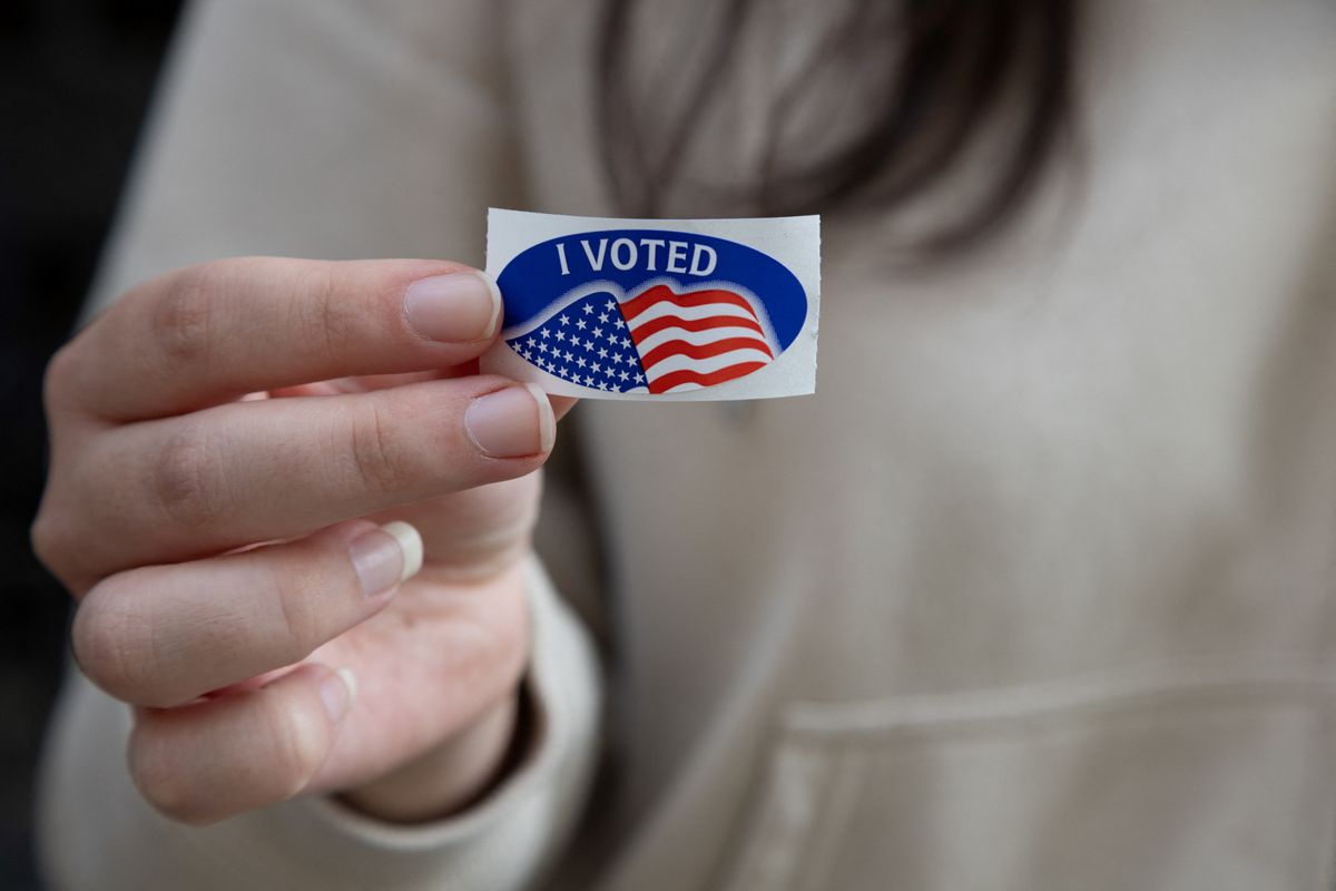 A person affixes an "I voted" sticker to their sweatshirt. 