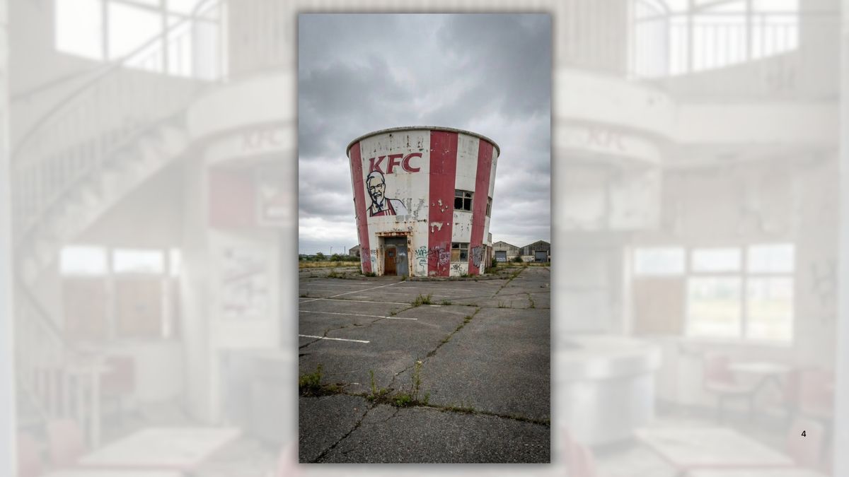 An AI-generated image of a KFC restaurant shaped like one of its buckets taken from the outside. It sits abandoned in an empty parking lot with little in the background. Windows are broken and/or partially boarded up.