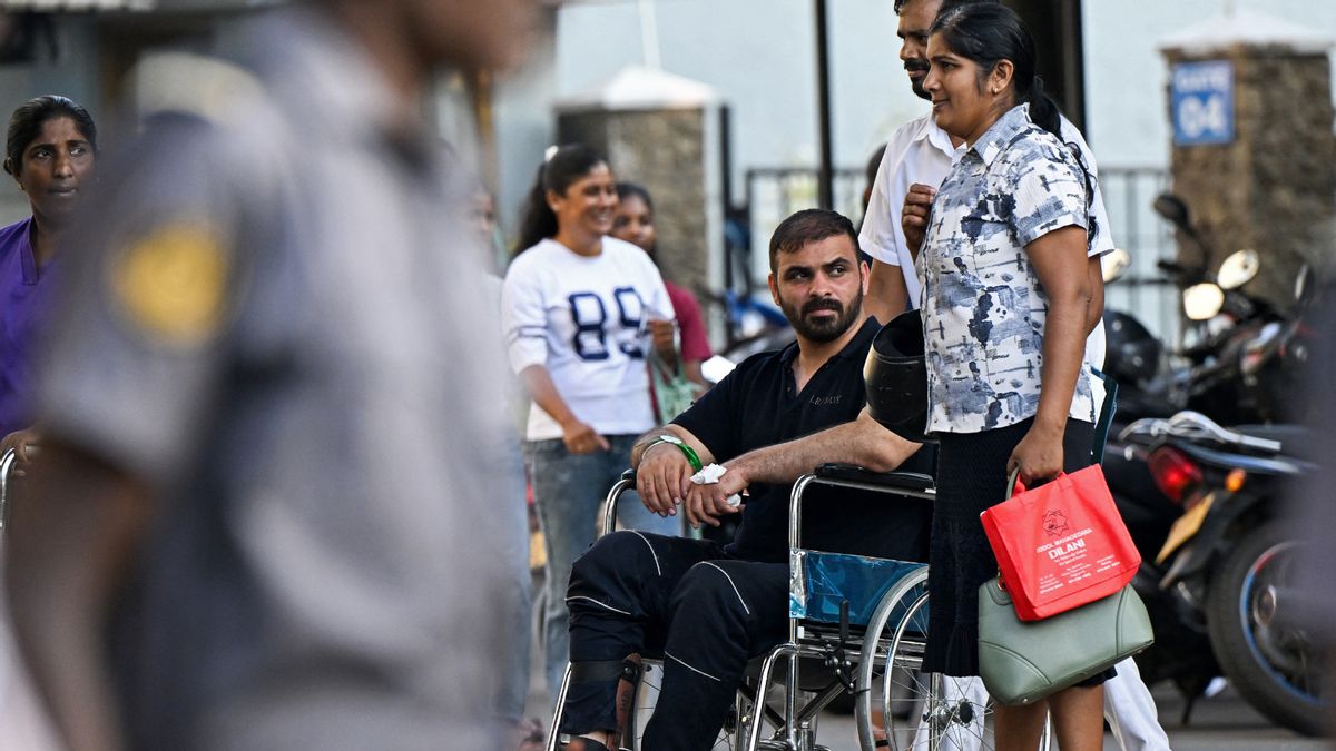 Image shows injured man in black shirt and pants in a wheelchair surrounded by other people