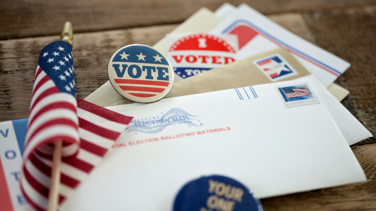Assorted voting pins, stickers and mail-in ballots alongside a United States flag. 