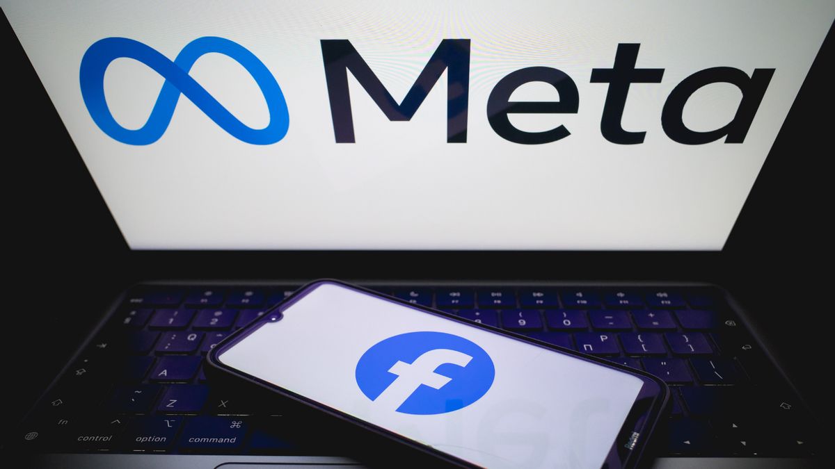 "Meta" logo appears on a laptop screen while a smartphone with the "Facebook" logo rests on the keyboard
