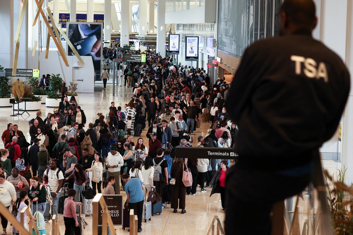 Image shows a TSA agent in uniform standing above a large crowd at an airport.