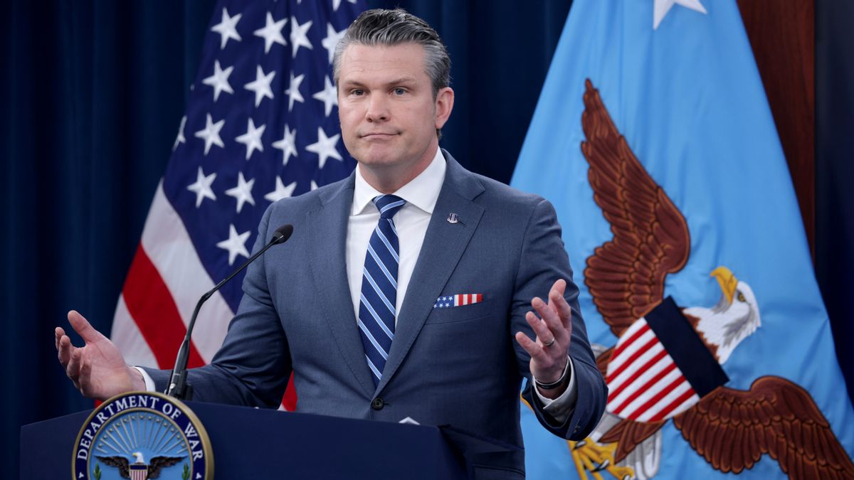 Defense Secretary Pete Hegseth, a white man with slicked back salt and pepper hair in a suit, stands in front of a podium and holds his hands in a shrug gesture.