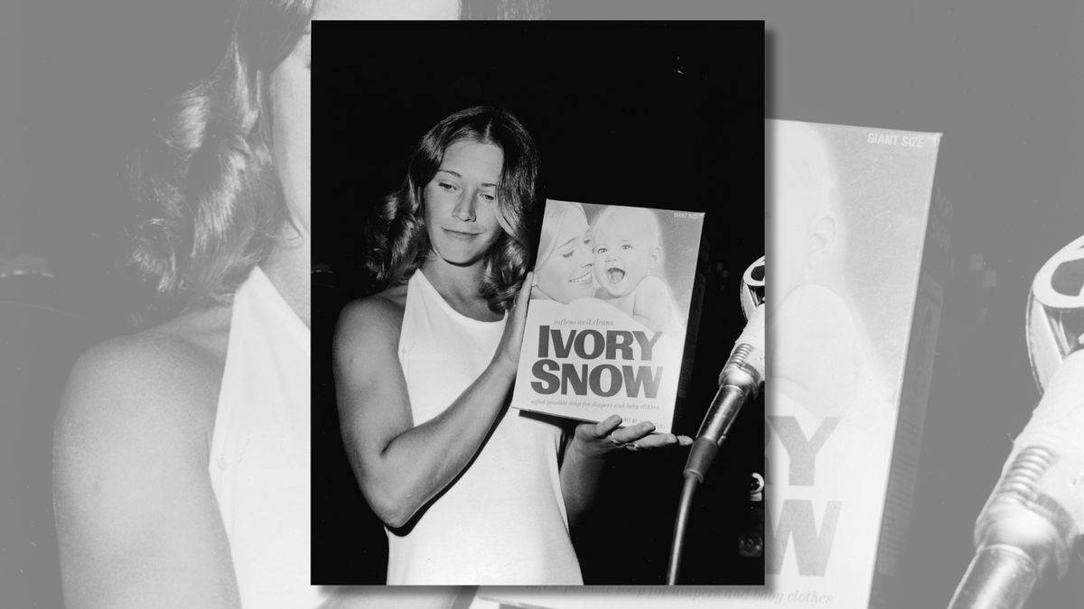 A black and white image shows a white woman holding a photo that shows her next to a smiling baby.