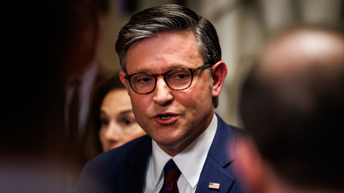 Close up photo portrait of Mike Johnson, a white man wearing glasses and a blue suit, talking to out-of-focus people in the foreground