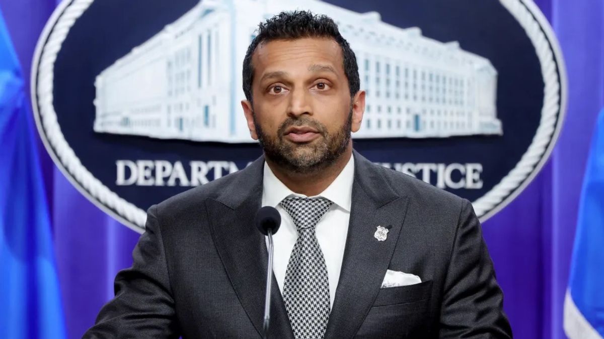 Kash Patel, who wears a black suit, with short black hair with a beard, speaks at a podium. Behind him, is a blue background containing the Department of Justice logo.