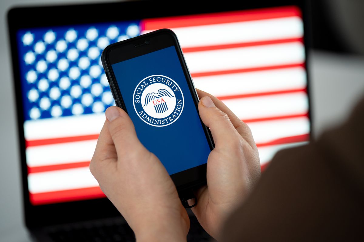 Image shows a hand holding a cell phone that reveals the Social Security Administration logo.