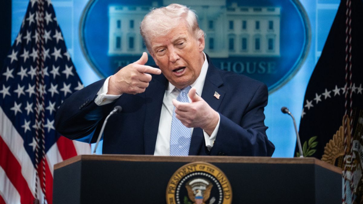 U.S. President Donald Trump, a tan, older white man in a suit, mimics firing a gun while standing behind a podium. 