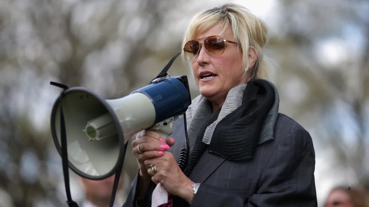 A white woman is shown speaking into a megaphone.