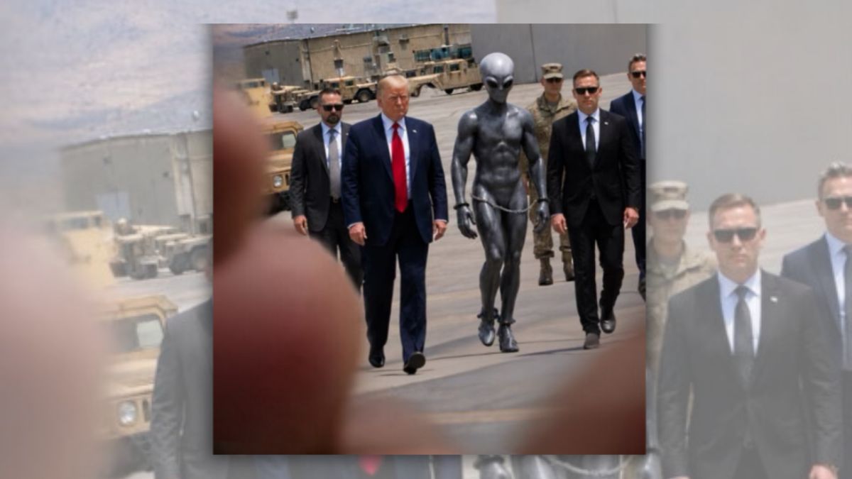A white man walks in a group of people either wearing suits or military uniforms. Next to him is a large blue-grey alien.