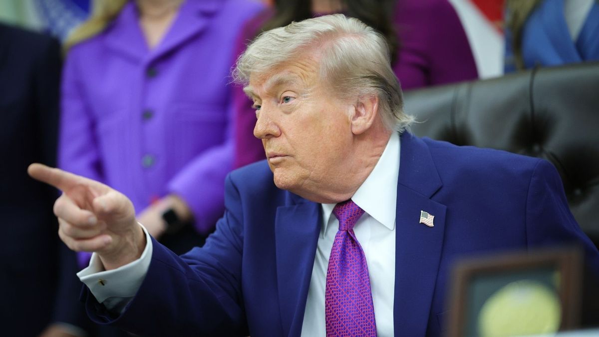 An image shows U.S. President Donald Trump sitting in the Oval Office in the White House pointing while wearing a suit and tie, and American flag pin.