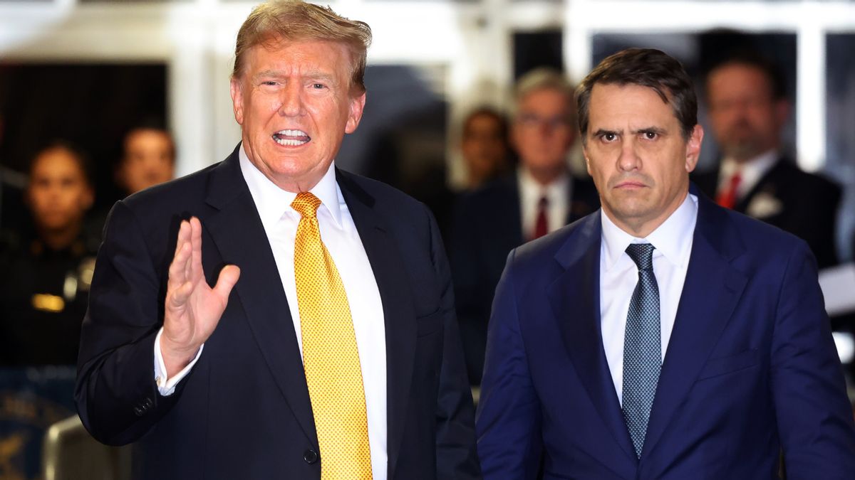 Donald Trump, a white man, wears a suit and yellow tie. Todd Blanche, a white man wearing a blue tie and blue suit jacket, stands to his right.