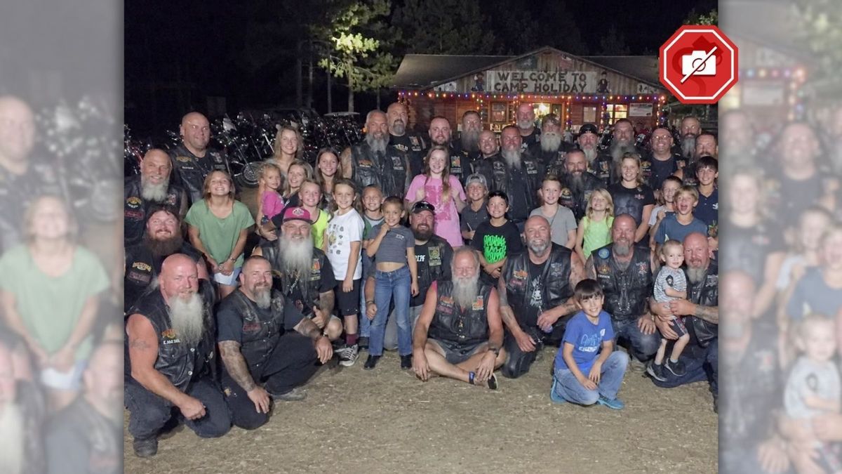 This image displays a fake, AI-generated glimpse at supposed bikers and children gathering at a camp, with the picture being taken at nighttime in front of a building with Christmas lights and a sign about Camp Holiday.