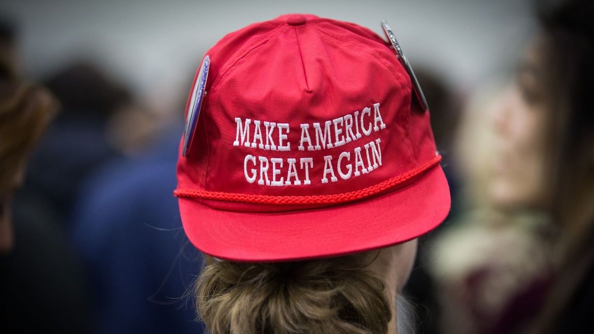 This image shows a close-up view from behind a person with long hair wearing a red Make America Great Again cap.