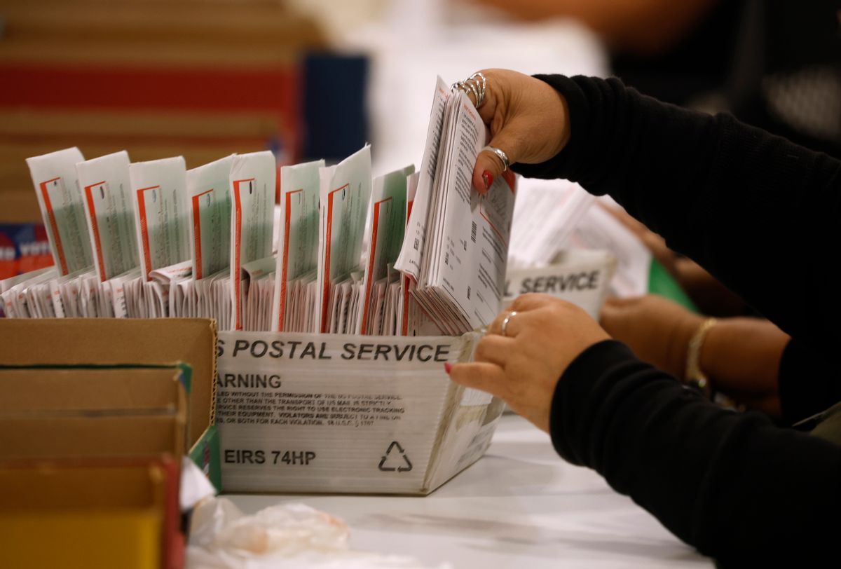 A worker's hands are seen placing a stack of mail-in ballots into a Postal Service container. 