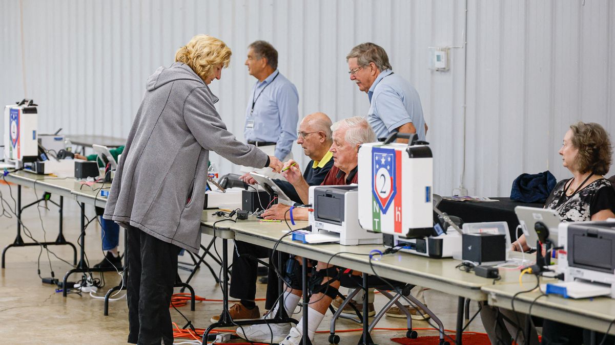 A woman with blonde hair and a gray coat vasts her vote at a polling place.