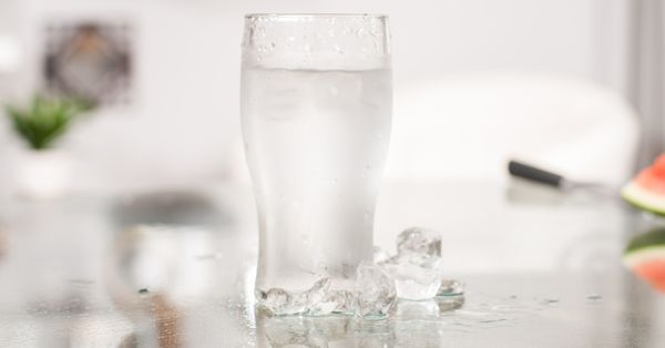 A glass of cold water with ice on a table.