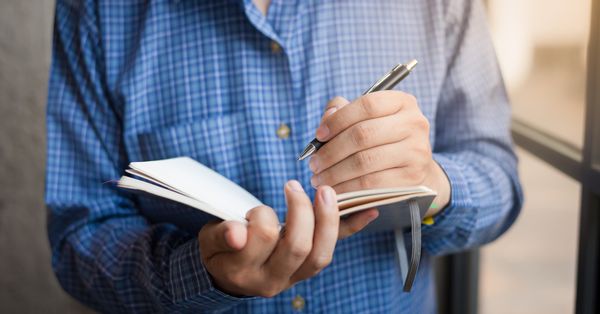 A left-handed man writing in a notebook.