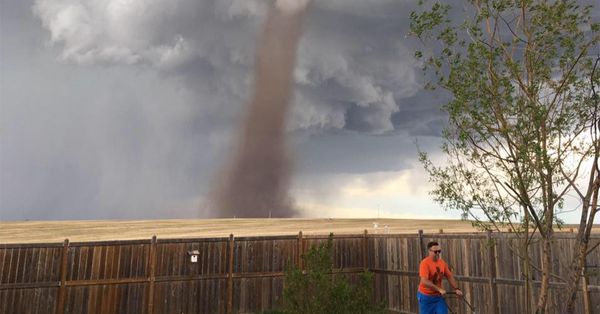 Man mowing his lawn while a tornado rages behind him
